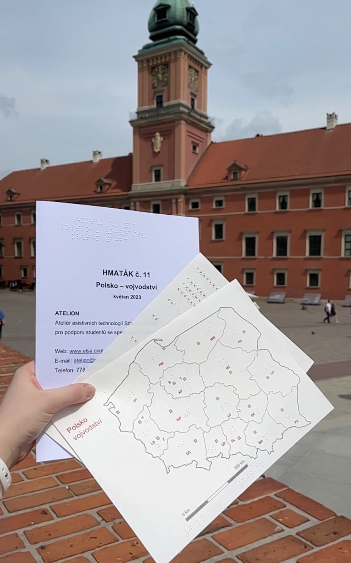 Obsah hmatáku č. 11 - desky, grafický list a seznam zkratek, na pozadí Zámecké náměstí ve Varšavě (Plac Zamkowy)
