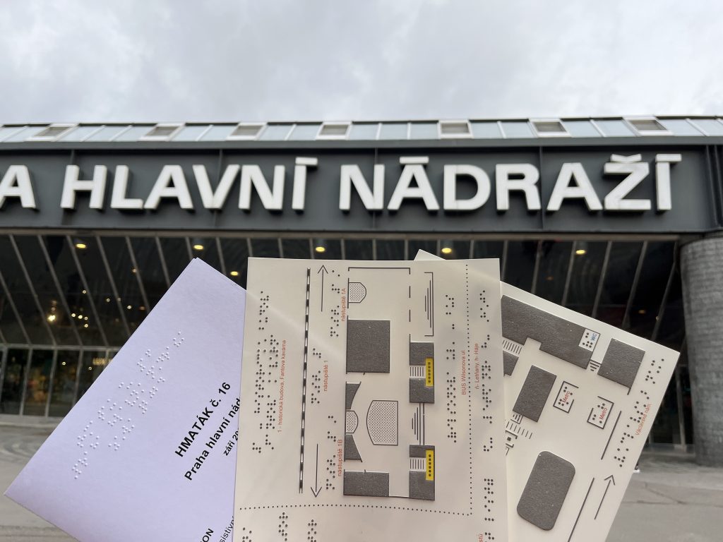 Desky hmatáku č. 16 Praha hlavní nádraží, na pozadí exteriér budovy hlavního nádraží.